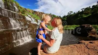 妈妈和小女孩一起坐在石头上，一起坐在瀑布旁
